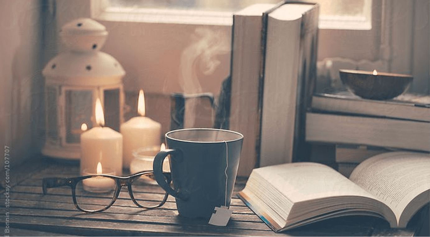 Cozy fiction writing scene with tea mug, open book, eyeglasses, candles, and stacked books
